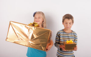 Siblings comparing their presents. The girl is happy with a big gift box while her bother having a small one is very upset.